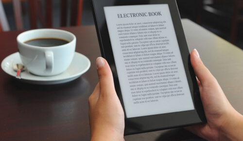 Hands holding e-reader displaying electronic book near coffee