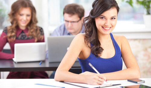 Smiling woman writing at desk with coworkers